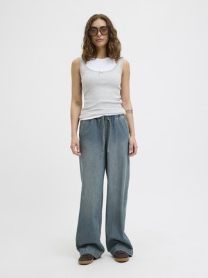 Light gray ribbed tank top layered over a white long-sleeve shirt, paired with loose blue denim jeans and brown slip-on shoes.