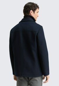 Giacca in misto lana blu navy con design strutturato, ampio colletto e linee pulite. Presenta una trama uniforme e dettagli di cucitura minimi.