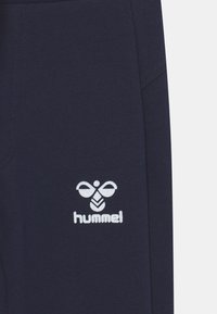 Kniehohe, navyblaue Sporthose aus weichem Material, mit einem weißen Hummel-Logo an der unteren linken Seite und einem schmalen, figurnahen Design.