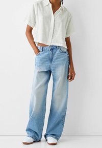 Przycięta biała lniana koszula z kołnierzykiem, zestawiona z luźnymi, jasnoniebieskimi dżinsami o wyblakłym wykończeniu i klasycznym zapięciu na guziki.