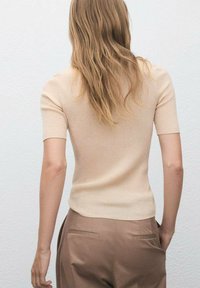 Top bej cu maneci scurte, cu un design mulat și guler rotund, asortat cu pantaloni maro cu talie înaltă, cu textură netedă și croială ajustată.