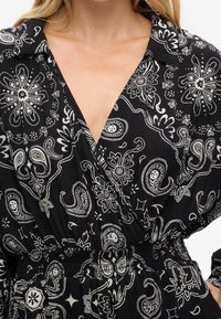 Vestido de patrón negro y blanco con cuello tipo camisa, diseño envolvente y cinturilla elástica. Incluye motivos florales y de paisley.