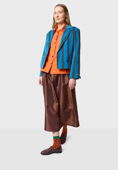 Raido sinitai bleiseri oranssilla paidalla, yhdistettynä kiiltävään ruskeaan hameeseen ja kuviollisiin oransseihin sukkiin. Ruskeat loafersit viimeistelevät asun.