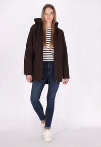 Giacca cappuccio marrone con cerniera frontale e tasche, abbinata a una maglietta a righe bianca e nera e jeans skinny blu, completata con sneaker bianche.