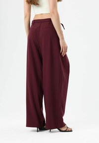Burgundy wide-leg trousers made of smooth fabric, featuring a high waist, two back pockets, and a drawstring detail at the waistband.