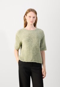 Textured short-sleeve sweater in light green, with a soft, fuzzy finish. Round neckline and relaxed fit, paired with black pants.