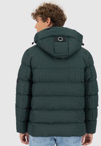 Giacca puffer verde scuro con una texture trapuntata, cappuccio regolabile e dettagli in hardware nero. Presenta cuciture visibili e una vestibilità comoda.
