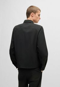 Zwarte, textuurrijke jas met een kraag, lange mouwen en knoopmanchetten, met een rechte snit en een minimalistisch ontwerp.