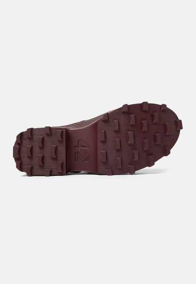 Dark maroon shoe sole with prominent rubber studs for traction, textured surface, and a central groove design. Features brand logo detail.