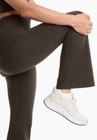 Leggings de sport marron au toucher lisse avec une coupe évasée, associés à des baskets beige clair avec un tissu texturé et une semelle blanche.