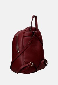 Sac à dos en cuir rouge avec une finition texturée, une forme ronde et une poche zippée extérieure. Il dispose de sangles réglables et d'une poignée supérieure.