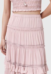 Falda de capas en rosa claro con bordes con volantes, detalles de encaje entre las capas y una cinturilla elástica. Textura de tela suave y fluida.