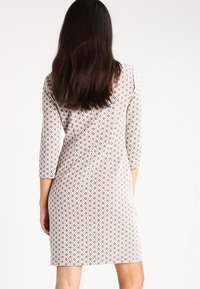 Robe à motif avec des manches trois-quarts, présentant un design géométrique en blanc et beige. Tissu lisse avec une silhouette ajustée.