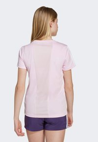 Pink athletic t-shirt with a mesh back panel, short sleeves, and decorative white stripes along the shoulders. Paired with dark purple shorts.