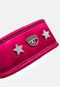 Fuksjowa saszetka z zamkiem błyskawicznym o gładkiej teksturze, z akcentami srebrnych gwiazdek i oczu na przodzie. Prosty, funkcjonalny design.
