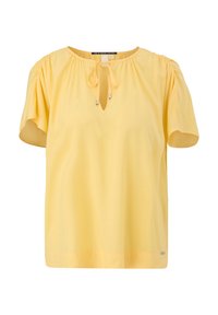 Blouse jaune à manches courtes avec épaules froncées et petit col en forme de goutte fermé par un ruban.
