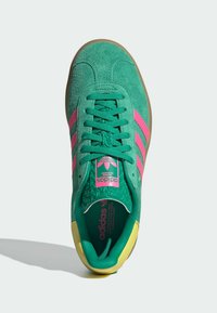 Gröna mockasko med rosa ränder, texturerad tunga och gula accenter; har snörning och vadderad innersula.