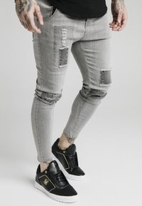Snygga grå denimjeans med slitna detaljer, lappar och fransade kanter, kombinerat med svarta sneakers med guldackenter.