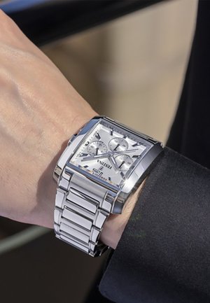 Montre-bracelet rectangulaire en acier inoxydable avec un cadran argenté, trois sous-cadrans et un bracelet poli. Dispose de repères horaires bien visibles et d'un affichage de la date.