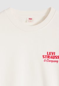 Camiseta blanca de ajuste relajado de Levi's con texto rojo "Levi Strauss & Company" en el pecho y etiqueta de talla dentro del cuello.