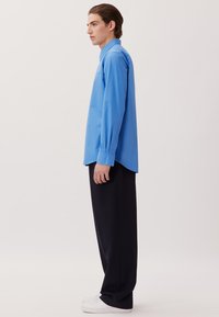 Himmelblaues Langarmhemd mit Kragen; kombiniert mit schwarzen Hosen und weißen Sneakers. Glatte Textur, lockerer Schnitt und gerades Design.