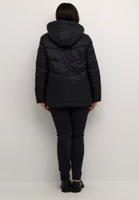 Giubbotto imbottito nero con cappuccio, caratterizzato da un design a pannelli diagonali e tessuto testurizzato. Abbinato a jeans scuri slim-fit e scarpe nere.