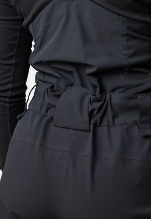 Black garment featuring a textured fitted top and loose lower section with gathered elastic waist and a patch detail, made from smooth fabric.