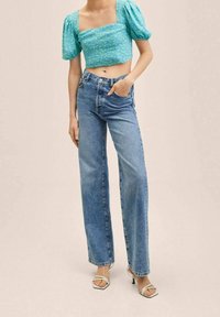 Helles blauen Blumen-Crop-Top mit Puffärmeln, kombiniert mit hoch taillierten, geraden Jeans und klaren Sandalen mit Absatz. Glatte Stofftextur.