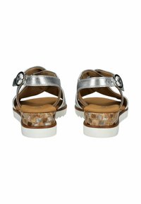 Sandalias metálicas plateadas con tiras cruzadas, hebilla ajustable y tacón cuadrado con textura de corcho. Suela de goma blanca y plantilla marrón.