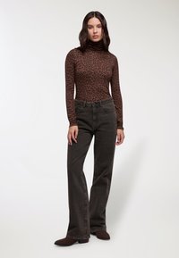 Maglione girocollo a stampa leopardata marrone abbinato a jeans a vita alta grigio scuro e stivaletti marroni. Texture liscia e design aderente.