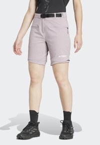 Person wearing light purple Terrex shorts with a black belt, black socks, black sneakers, and a black top against a white background.