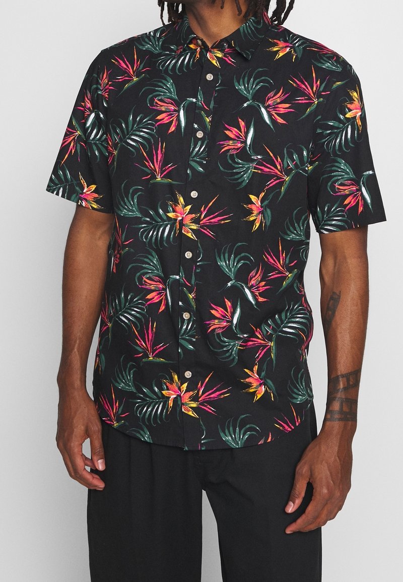 Camisa de botones de manga corta en tela negra con un vibrante patrón floral tropical en rosa, naranja y verde. Presenta un cuello y botones de perlas.