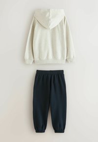 Lysegrå hættetrøje med snor i hætten og ribbede manchetter, parret med navy joggers, der har elastisk talje og smalnede ankler.