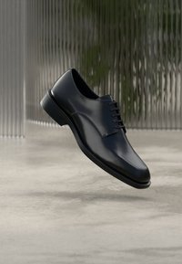 Chaussure habillée en cuir noir avec une surface lisse, un bout rond et un laçage traditionnel. La semelle présente une légère brillance et une finition polie.