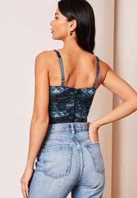 Body in navy arricciato con un motivo astratto blu chiaro, dotato di spalline regolabili e zip sulla schiena. Abbinato a jeans in denim a vita alta.