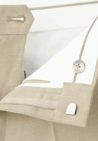 Tela de lino beige con un detalle blanco, cierre de botón y detalle de aro metálico. Textura suave con costuras visibles.