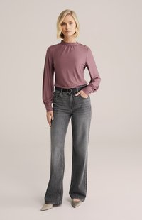 Dugih rukava ljubičasta bluza s visokim ovratnikom i ukrasnim gumbima, uparena s visokim strukom, širokim sivim trapericama i šiljastim bež potpeticama.