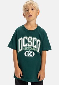 Zelené bavlněné tričko s výrazným bíl ým a světle zeleným nápisem "DC Shoe Company" a "094". Krátké rukávy a kulatý výstřih.