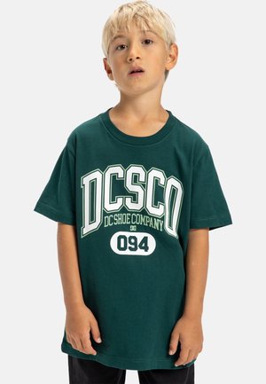 Grön bomull t-shirt med fet vit och ljusgrön text "DC Shoe Company" och "094." Korta ärmar och rund halsringning.