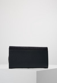 Svart clutchväska med texturerad yta, med en glittrande överpanel och en kedjelänkdetalj på sidan. Rektangulär form, elegant design.