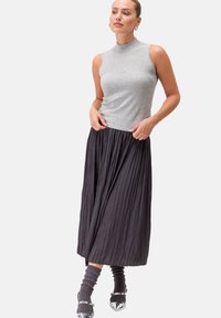 Top grigio senza maniche, gonna maxi nera plissettata, calze grigie fino al ginocchio e scarpe argentate. Tessuto liscio e gonna texturizzata con pieghe visibili.