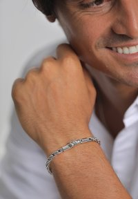 Silverarmband med en vriden kedjedesign och cylindriska metallaccenter. Ytan har en polerad finish mot huden.