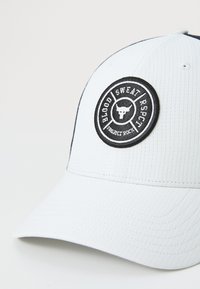 Hvid kasket med ribbet tekstur, udstyret med et cirkulært sort mærke med "BLOOD SWEAT RESPECT" og et stykke grafik af en tyr i midten.