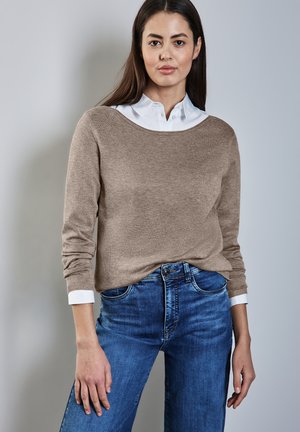 Ljust brunt stickat tröja med vid halsringning, bärs över en vit skjorta med krage, ihop med blå denimjeans. Mjuk textur, avslappnad passform.