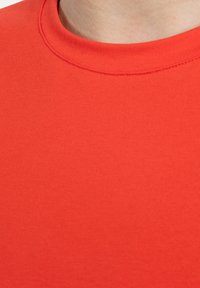 Camiseta de algodón roja con cuello redondo y textura suave, que presenta un color uniforme sin patrones ni adornos.