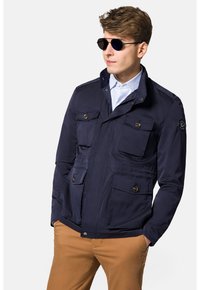 Granatowa, lekka kurtka z zamkiem błyskawicznym i zapięciem na guzik, cztery przednie kieszenie i stójka. Gładka faktura i nowoczesny design.