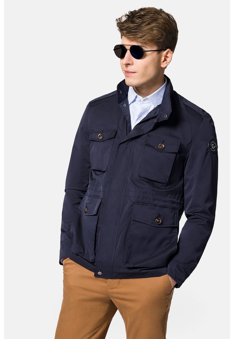 Granatowa, lekka kurtka z zamkiem błyskawicznym i zapięciem na guzik, cztery przednie kieszenie i stójka. Gładka faktura i nowoczesny design.