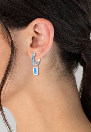 Pendientes de aro de plata con una piedra rectangular azul. El aro presenta pequeñas piedras azules de acento a lo largo de su curva.