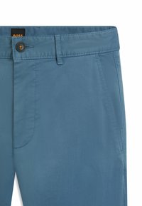 Světle modré kalhoty z hladké látky s knoflíkovým zapínáním, poutky na pásek a bočními kapsami. Mají jemné detaily šití.