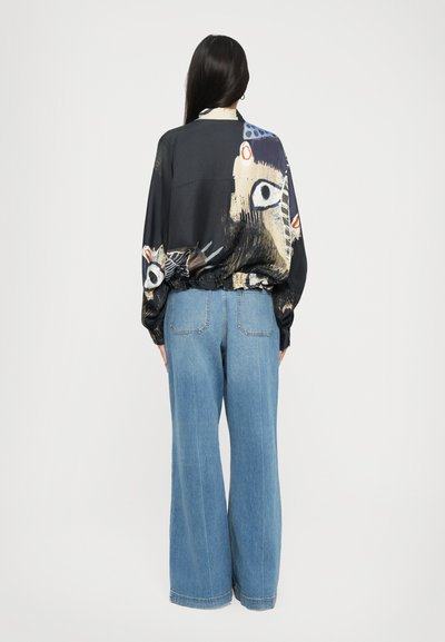 Black shirt with colorful abstract patterns, long sleeves, and elastic hem paired with wide-leg blue denim jeans.